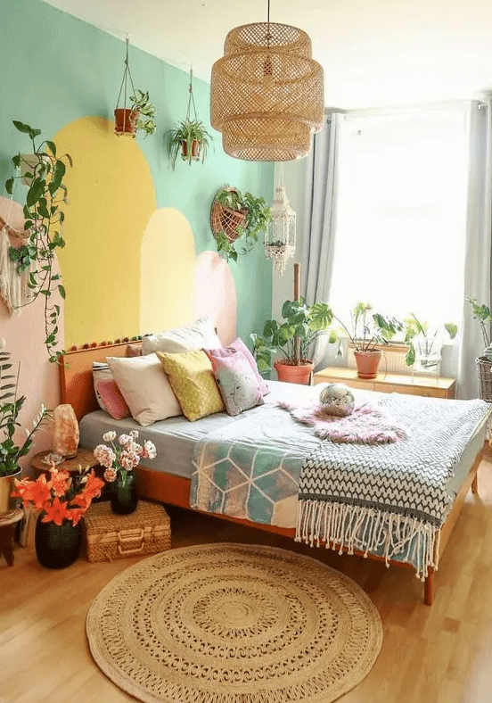a dopamine decor bedroom with a cool and colorful accent wall, a bed with pastel bedding, blooms, a pendant lamp and greenery