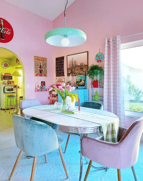 a dopamine decor dining room with blush walls, a table and turquoise and lilac chairs, a bold gallery wall and a green pendant lamp
