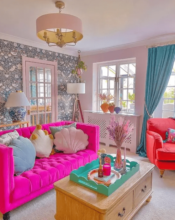 a dopamine decor living room with a wallpaper wall, a hot pink sofa with pastel pillows, a coral chair and blue curtains