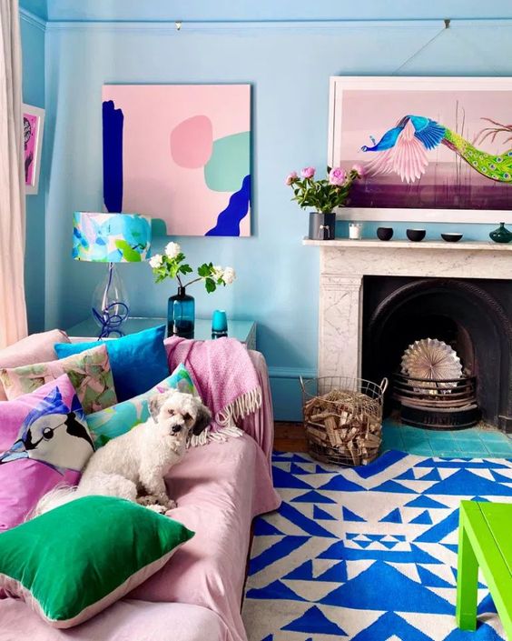 a dopamine decor living room with blue walls, a fireplace, a pink sofa with bright pillows, some bright artwork and a bold green table