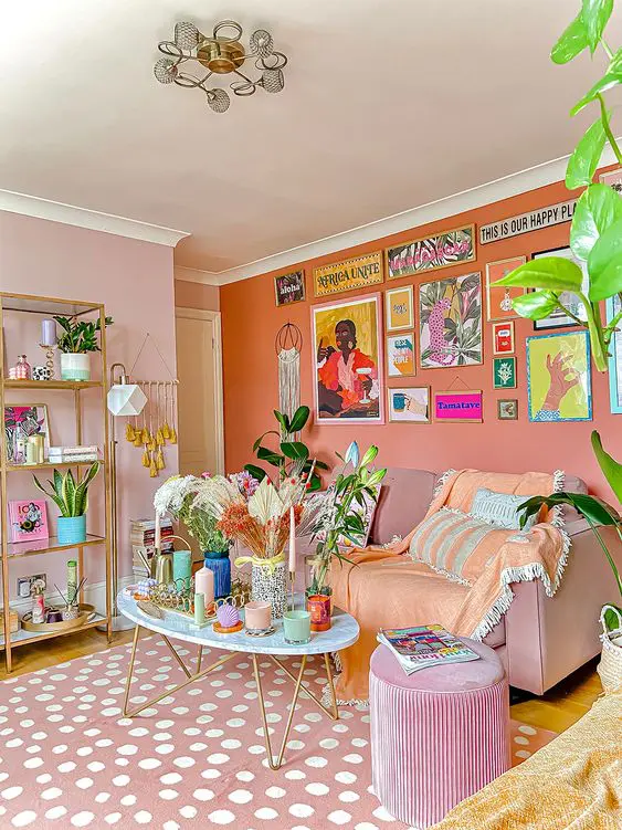 a dopamine decor living room with blush and an orange accent wall, a blush sofa and a pouf, a coffee table with decor and a bright gallery wall