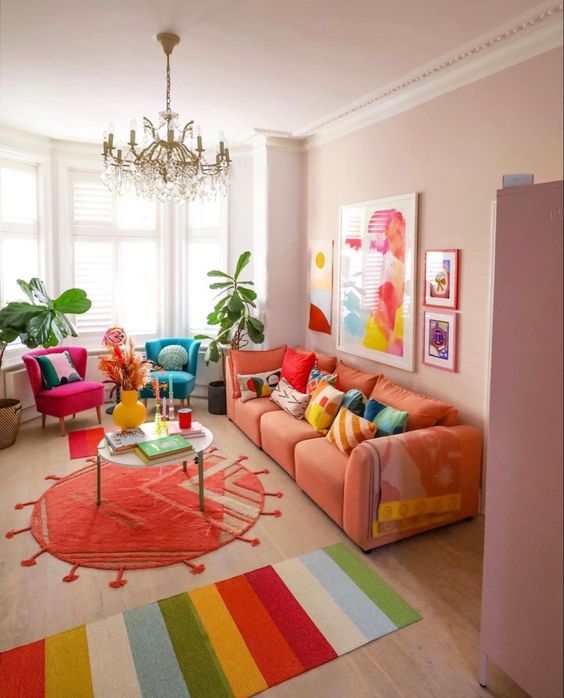 a dopamine decor living room with blush walls, an orange sofa with colorful pillows, bright rugs and bold chairs
