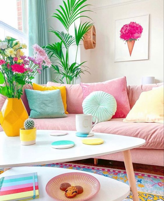 a dopamine decor space with a pink sofa and colorful pillows, a tiered coffee table with bright decor and blooms