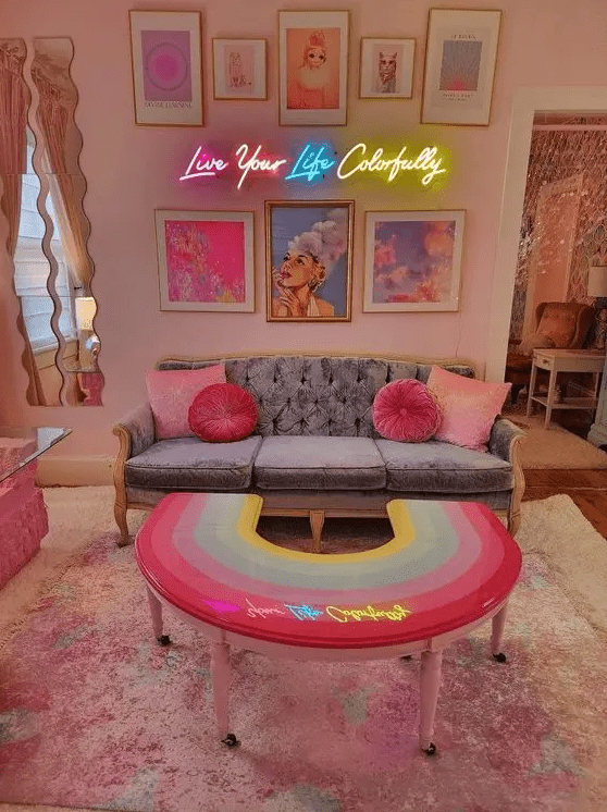 a dopamine living room with blush walls, a grey sofa with pink pillows, neon lights and a bright gallery wall