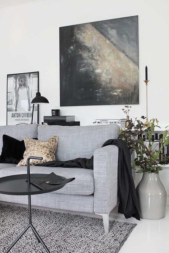 a dramatic living room with a grey sofa and pillows, a console table with books, a coffee table and art, black touches bring drama here