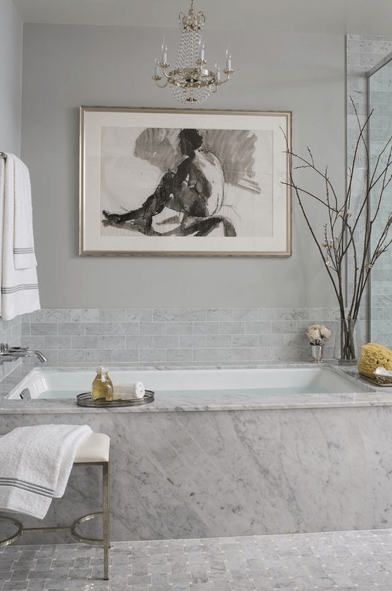 a fancy bathroom with grey marble tiles and marble itself, a crystla chandelier and a bold statement artwork just wows