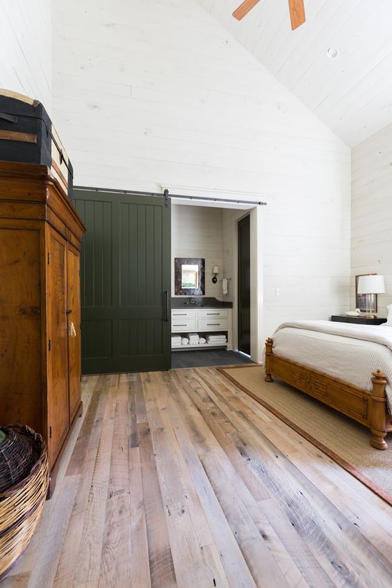 a farmhouse bedroom with an en-suite bathroom hidden behind a dark green barn door that creates a dramatic look