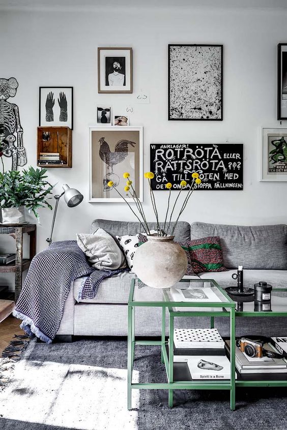 a fun and cool living room with a grey sofa and pillows, a grey rug, green frame coffee tables, a whimsical gallery wall and greenery