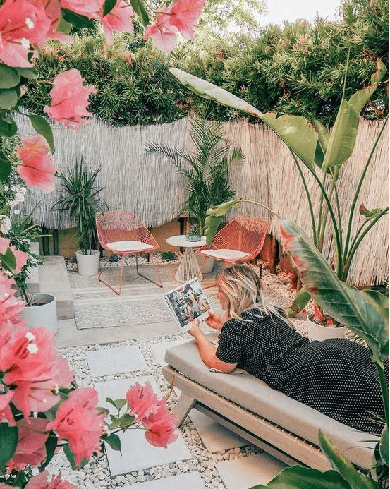 a gorgeous tropical patio with pink chairs and pink blooms, a comfy daybed, potted tropical plants