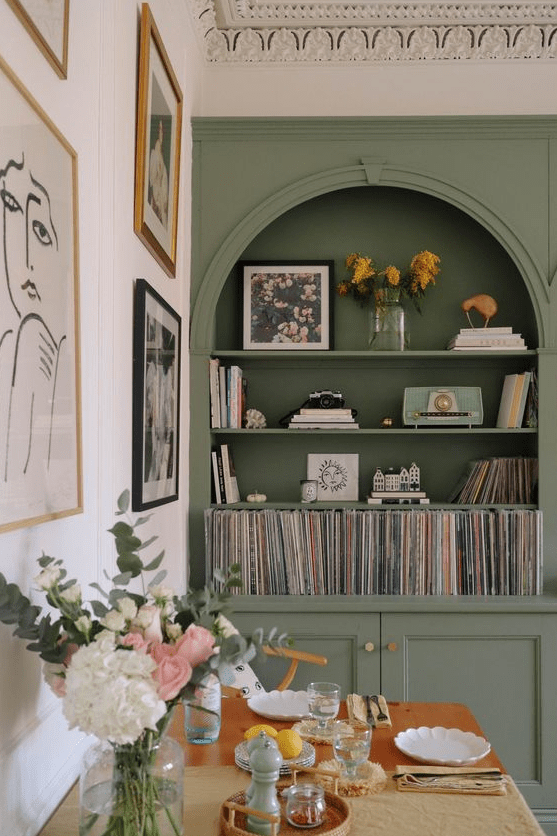 a green built-in arched bookcase, a dining table, chairs and a gallery wall, some blooms and decor are amazing