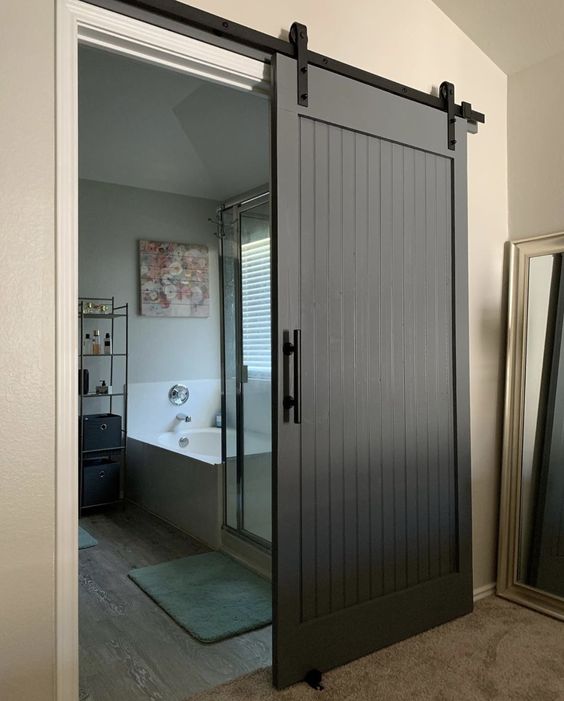 a large black barn door hiding a large bathroom is a cool solution for a farmhouse space or other rustic room