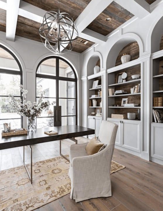 a large home office with arched windows and arched bookcases that echo with them, a desk, a white chair and a sphere lamp