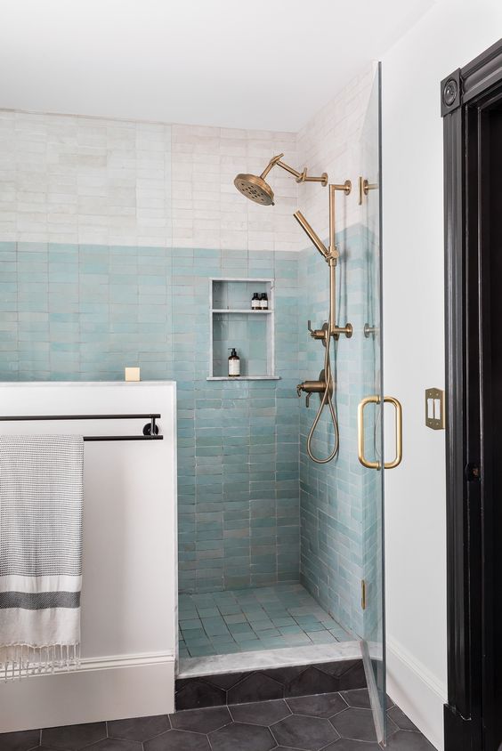 a large shower space clad with white and aqua skinny Zellige tile, brass hardare and a niche shelf is amazing