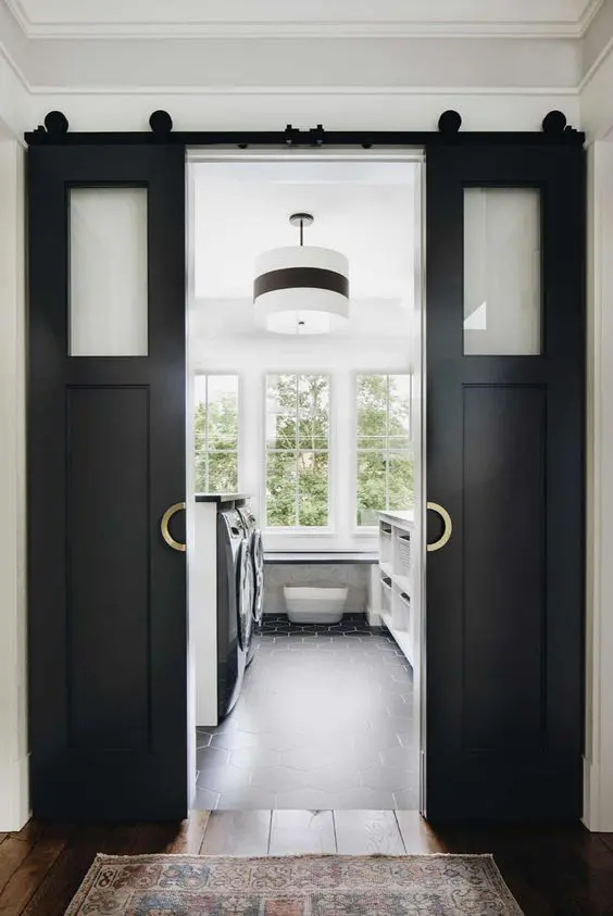 a laundry hidden under small black barn doors with glass panes is a cool idea, such doors will add to any farmhouse space