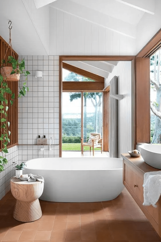 A light filled bathrom with glazed walls, a tub, terracotta and usual tile, a vanity and greenery feels very natural