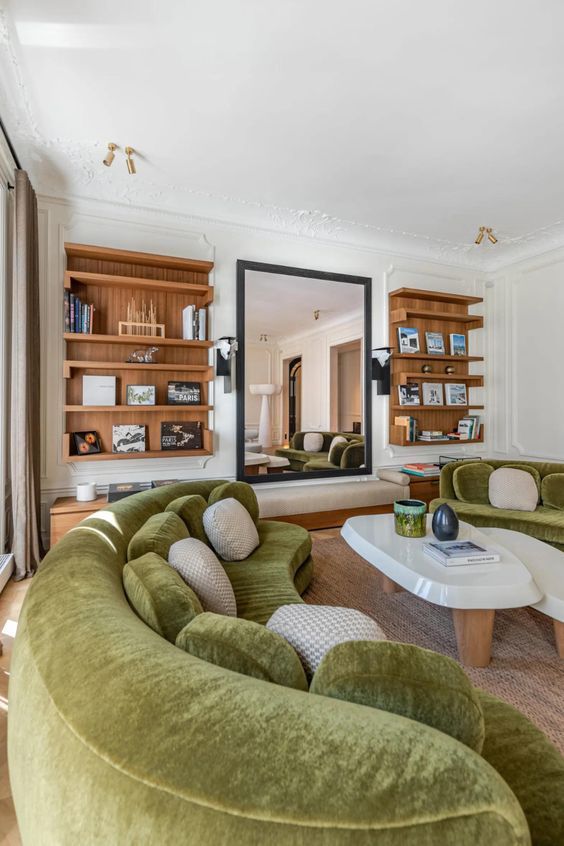 A living room with built in bookshelves, a large mirror and a bench, green curved sofas and coffee tables is amazing