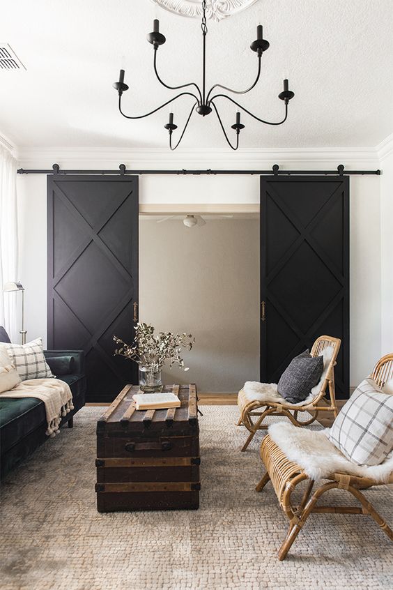 a lovely farmhouse space with a dark green sofa, rattan chairs, a chest as a coffee table and black barn doors