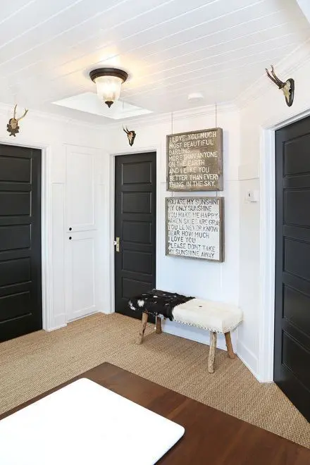 a lovely farmhouse space with white walls, black doors, a cowhide bench, antlers and layered rugs plus rustic signs