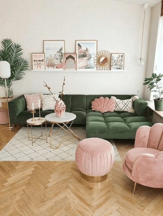 a lovely living room with a green sectional, a pink chair and a pouf, some pillows, a ledge gallery wall and potted plants