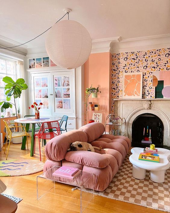 a lovely open layout with wa;;[a[er walls, a fireplace with colorful candles, a pink sofa, a printed rug and colorful chairs