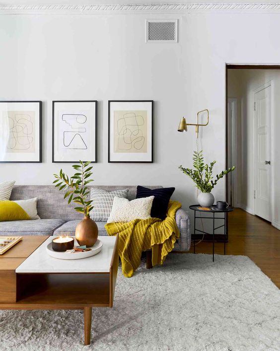 a mid-century modern living room with a grey sofa, a coffee table, a side table and a gallery wall, greenery and mustard touches