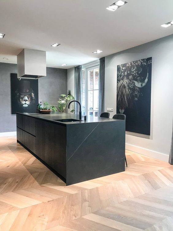 a minimalist kitchen with grey walls, a black stone kitchen island, a chevron floor, some statement artwork and lights