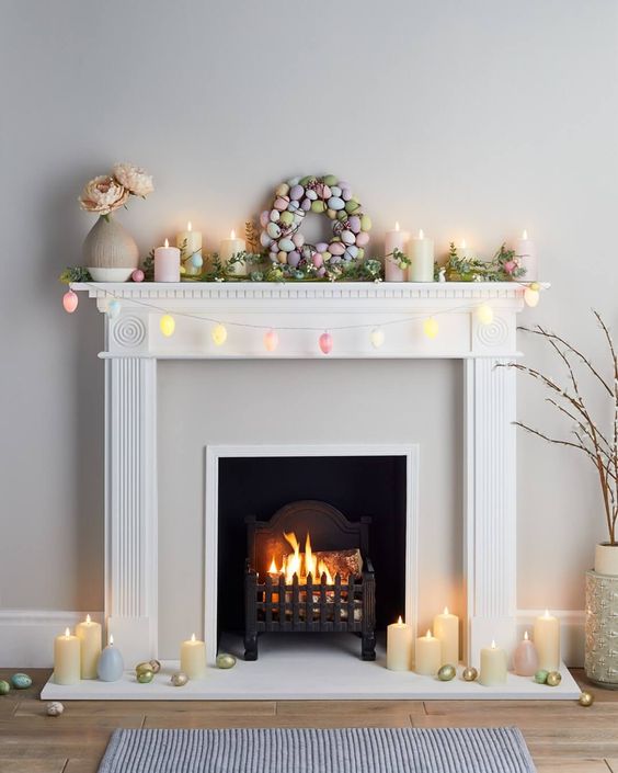 a modern Easter mantel with egg-shaped lights, greenery, a pastel egg wreath, candles and a vase with faux blooms