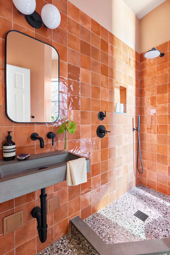 a modern bathroom clad with bold glazed terracotta tiles, a terrazzo floor, a shower, a concrete sink and black hardware