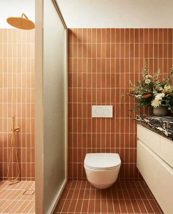 a modern bathroom clad with skinny terracotta tiles, a shower space, a white vanity, a glass space divider