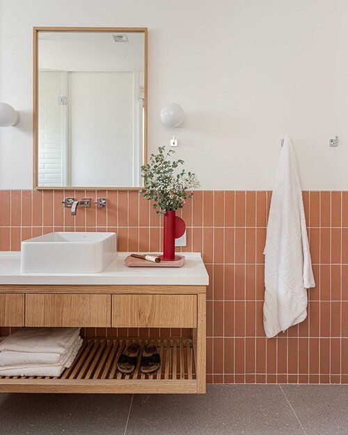 a modern bathroom clad with terracotta tiles, a stained vanity, a sink and a mirror in a gold frame
