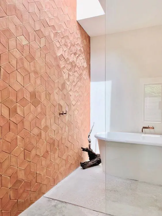 a modern bathroom done with neutral terrazzo, a terracotta tile wall, a tub and a piece of driftwood as decor