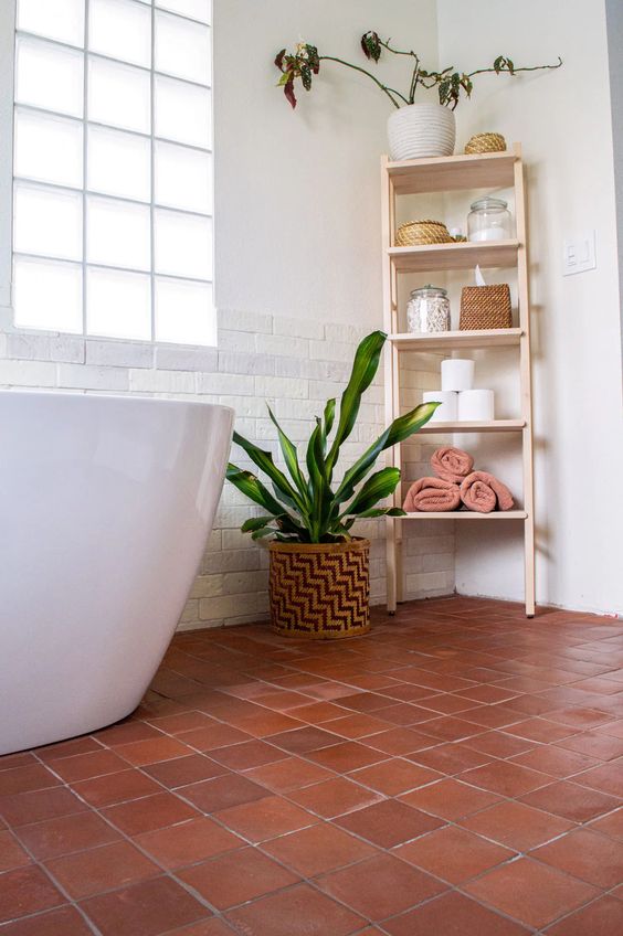 a modern bathroom done with skinny faux bricks, glazed terracotta tiles on the floor, a shelving unit and potted greenery