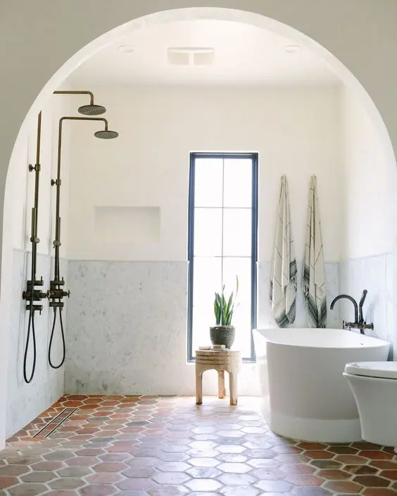 a modern bathroom with a terracotta tile floor, white marble panels, a tub, a shower space and a stool by the window