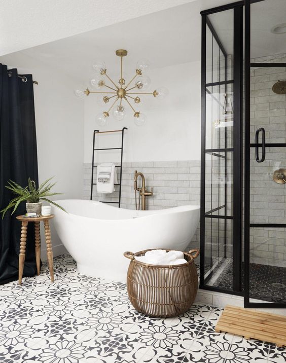 a modern bathroom with marble and printed tiles, a shower space, a tub, black curtains, a gold chandelier and some decor