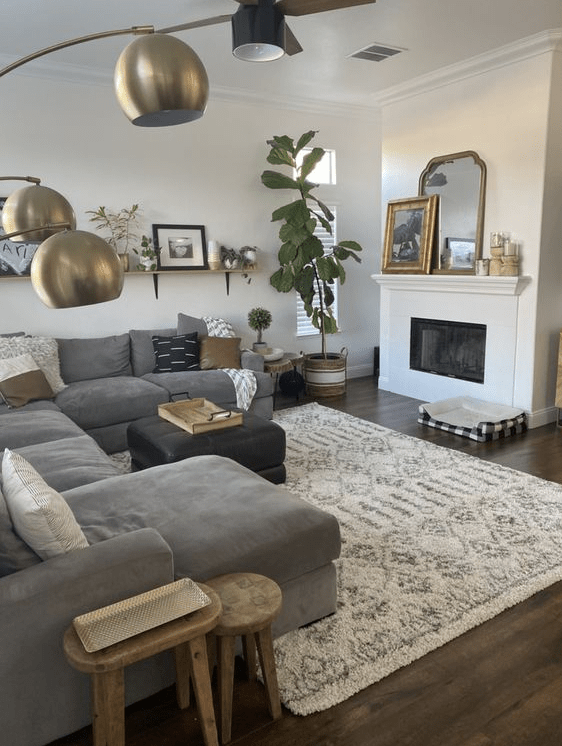a modern boho living room with a fireplace, a grey sofa with pillows, stools, potted plants, shelves with decor and a mirror