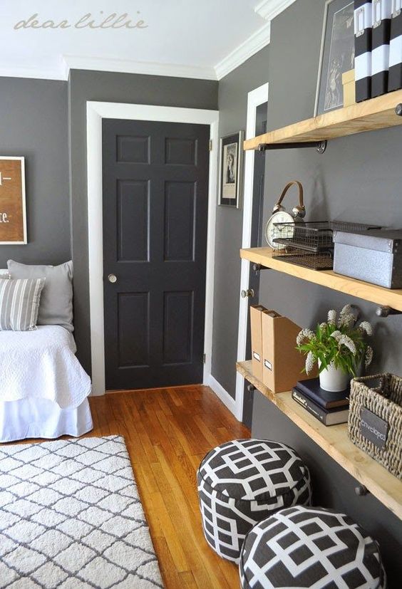 a modern farmhouse room with grey walls, a black door, open shelves, printed poufs and a bed with neutral bedding