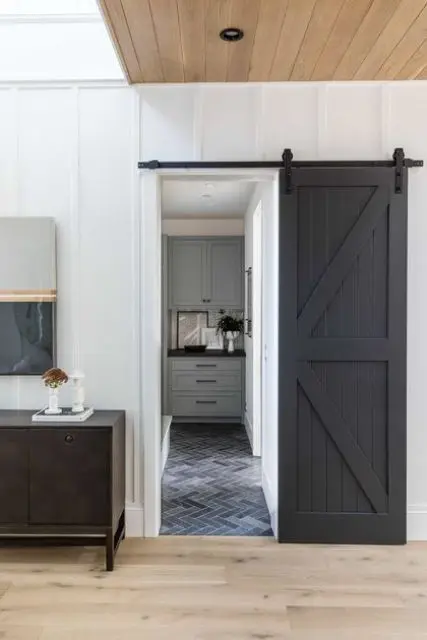 a modern farmhouse space with a black barn door that hides a bathroom, a dark credenza and some lamps and art