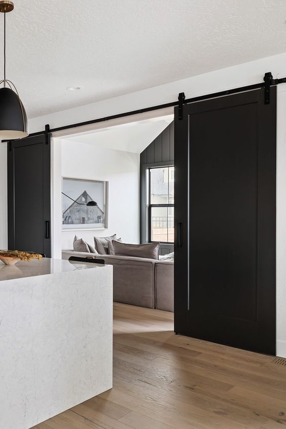 a modern farmhouse space with black barn doors, stylishneutral furniture and black pendant lamps that echo with the doors