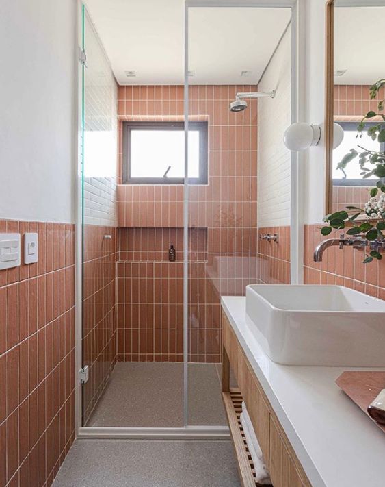 A modern light filled bathroom clad with terracotta tiles, a stained vanity, a shower with a window and some greenery