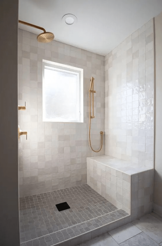 a modern neutral bathroom clad with neutral zellige tiles, stone ones on the floor, brass and gold fixtures
