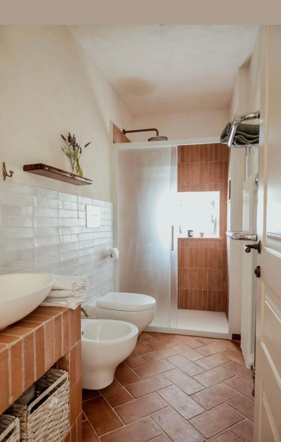 a modern rustic bathroom done with white skinny and terracotta tiles, a terracotta clad vanity, a shower and black fixtures