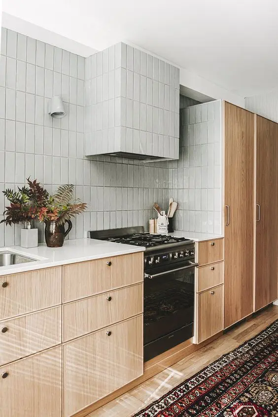 a modern stained kitchen with white stone countertops, a grey Zellige tile wall and a hood is a creative and chic space
