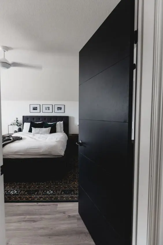 a modern to boho bedroom with a black bed, a printed boho rug, stained nightstands and a large black door to add contrast