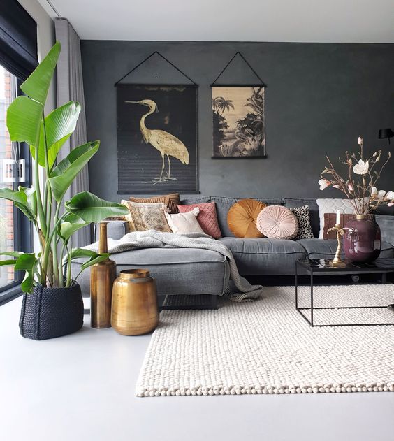 a moody living room with a graphite grey accent wall, a grey sofa with bright pillows, a potted plant, a coffee table and a neutral rug