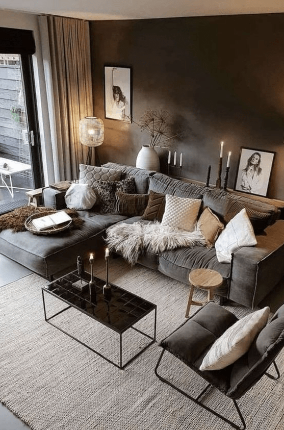 a moody living room with a graphite grey wall, a grey sofa and a chair, a black coffee table and lots of pillows and candles
