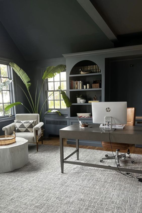 a moody soot home office with an arched bookcase, a desk, a chair, a white chair with a stump coffee table