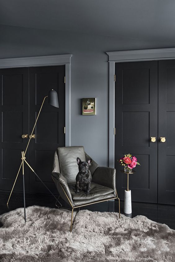 a moody space with black doors, gold hardware, a black and gold floor lamp, a grey rug and a grey chair is a chic one