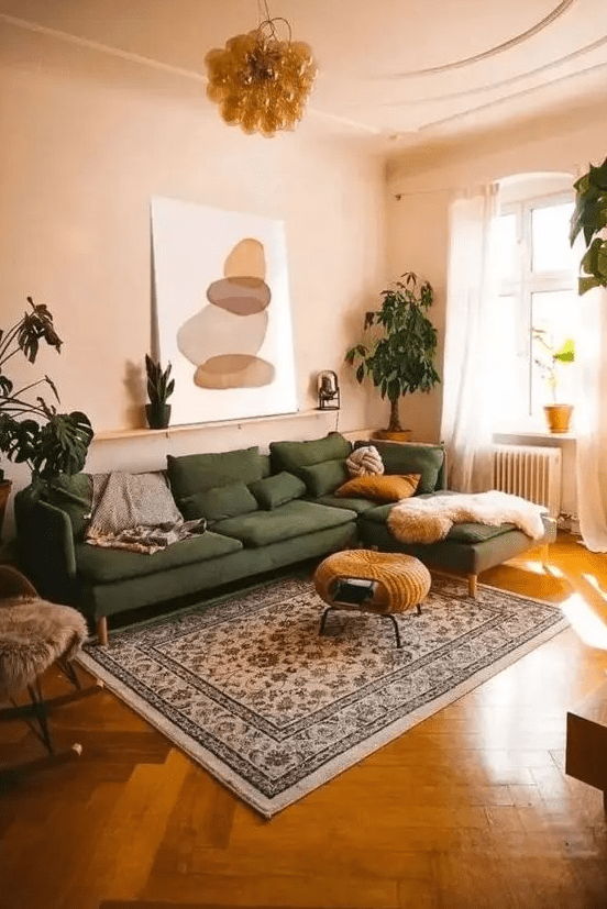 a muted and warm-colored living room with tan walls and a ceiling, a green sectional, a woven pouf, a printed rug and potted plants