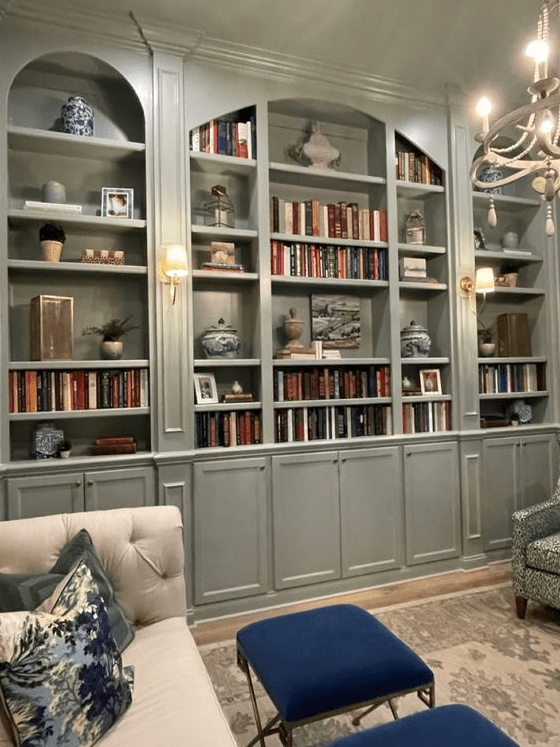 a neutral living room with grey green arched bookcases, a neutral sofa with pillows, navy stools