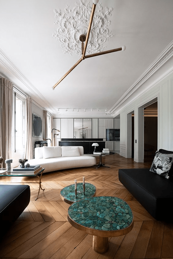 a open layout with parquet floors, a white sofa and a black loveseat and ottoman, coffee tables and a creatie chandelier